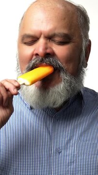 Indian Asian senior businessman with a white beard, holding a candy ice cream cone, feeling sudden toothache shows discomfort on face