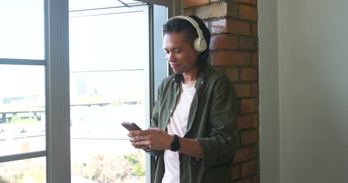 African American man holding phone with white headphones by window reacting to audio, copy space