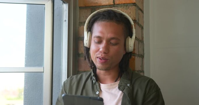 Man sitting by metal window and brick column, responding to tablet content, laughing and speaking