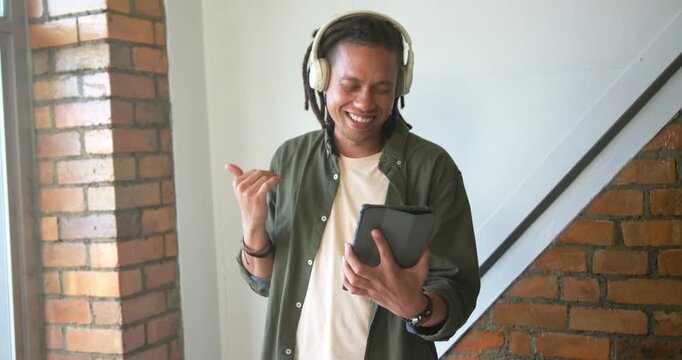 Adult male in loft wearing headphones and holding tablet, following audio, nodding and fist-pumping