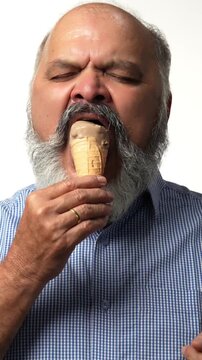 Indian Asian senior businessman with white beard savoring a chocolate ice cream cone, enjoying a casual moment  of joy and relaxation
