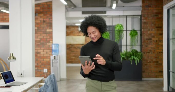 African American man starting tapping tablet, smiling, looking up and walking in office with laptop