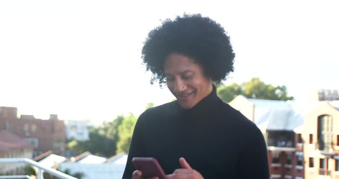 African American man lifting smartphone, tapping, scrolling, reading messages on rooftop balcony
