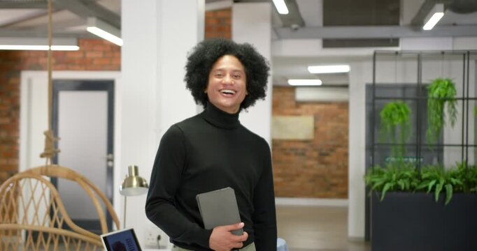 African American man holding tablet, smiling and adjusting pose after camera prompt at office