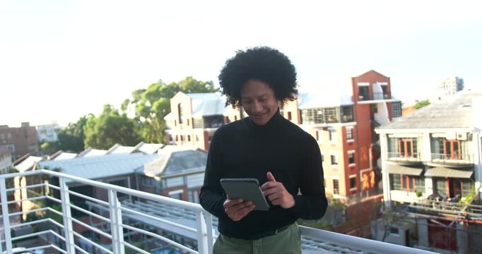 Man starting by tapping tablet while standing on balcony in turtleneck, glancing for work