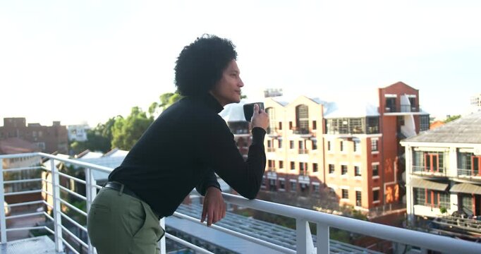 African American man leaning on metal railing lifting mug to sip prompted by bright sunlight