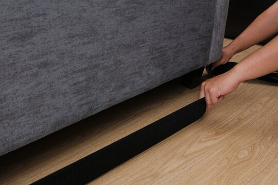 A high-quality commercial lifestyle product photograph captured from an angled close-up perspective. A person's hands are actively installing a wide black fabric toy blocker strap around the leg.