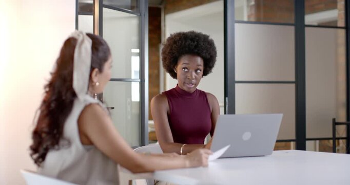 Female team left sliding paper, right woman reading, reviewing, typing on laptop in conference room