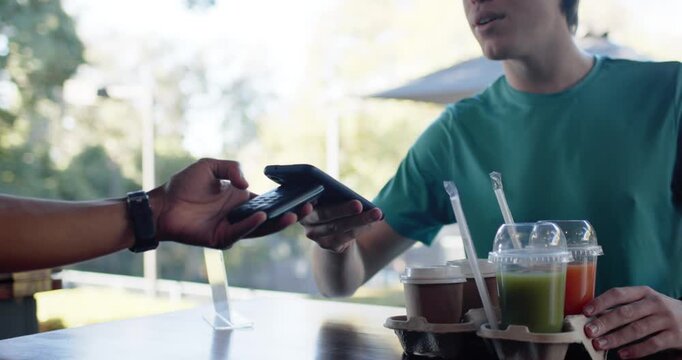 Male in teal tee tapping phone, paying as server offering card reader at patio, steadying carrier