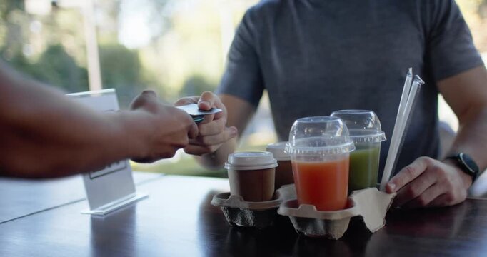 Diverse customer-server tapping phone at reader to pay, server in gray t-shirt handing three drinks