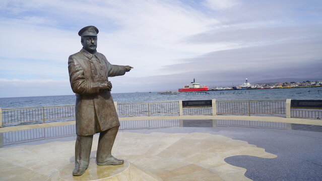 Bronze statue of Chilean Navy officer Captain Luis Pardo Villal&oacute;n pointing toward the Strait of Magellan along the costanera boardwalk, with ships anchored in the background