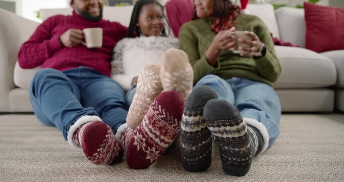 African American family on carpet, child wiggling patterned socks, parents smiling and sipping mugs