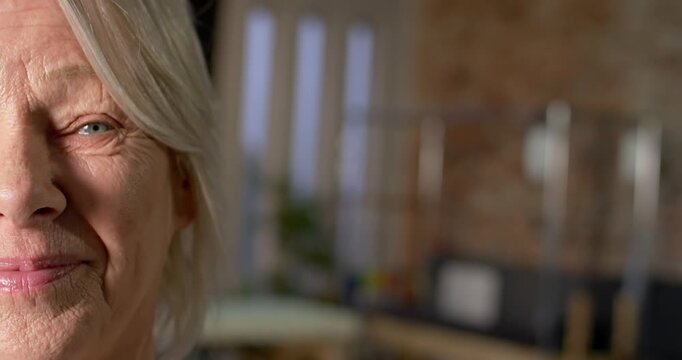 Mature woman holding slight smile while camera recording in studio with tall windows, copy space