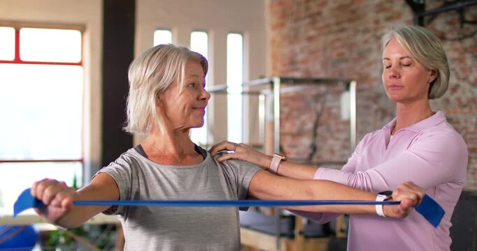 Senior female client with trainer touching shoulder as client pulling elastic band for rehab in gym