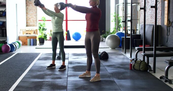 Two female friends swinging kettlebells, driving hips forward, syncing reps for fitness in studio