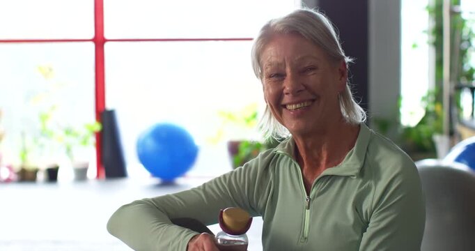 Senior woman green-top holding bottle with wooden-ball, smiling while camera tightening at gym