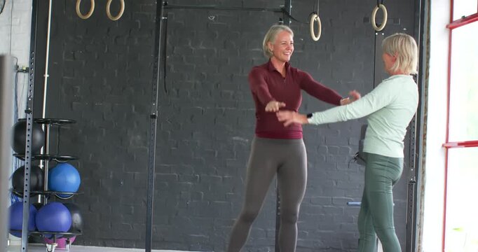 Female workout partners exchanging palm high-five, encouraging touches, flexing, smiling near rig