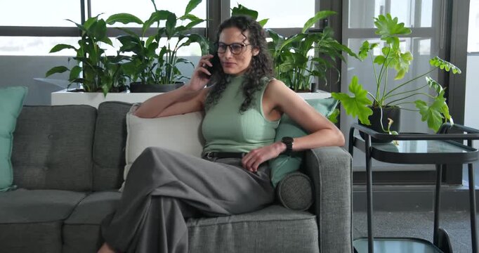 African American woman in top entering office lounge on smartphone, placing laptop, typing for work