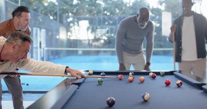 Diverse male friends watching shooter lining and striking cue ball at pool table during casual game