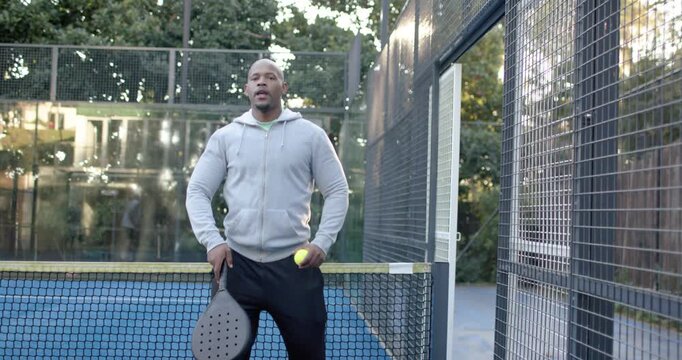 African American man spotting ball at net, bending, retrieving and warming with racket for play