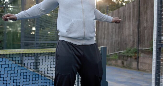 African American man stretching arm across chest while straddling court net, wearing hoodie