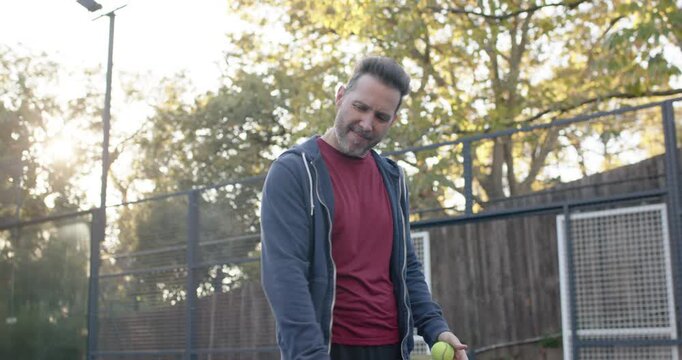 Adult man inspecting paddle, producing yellow ball, testing balance and practicing swings on court
