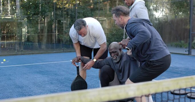 Diverse men helping African American senior man rising from court crouch, holding paddle to walk