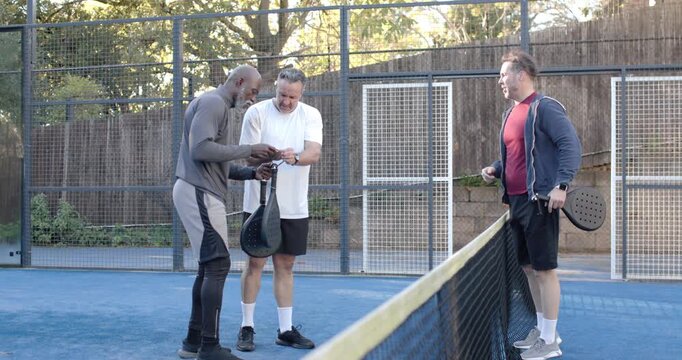 Diverse male friends in gear meeting at net, checking paddles, untangling strap preparing for match