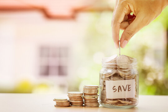 Hand dropping coin into glass jar labeled save representing long term financial savings goal success