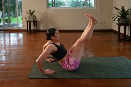 Woman lifting one leg while balancing on yoga mat indoors