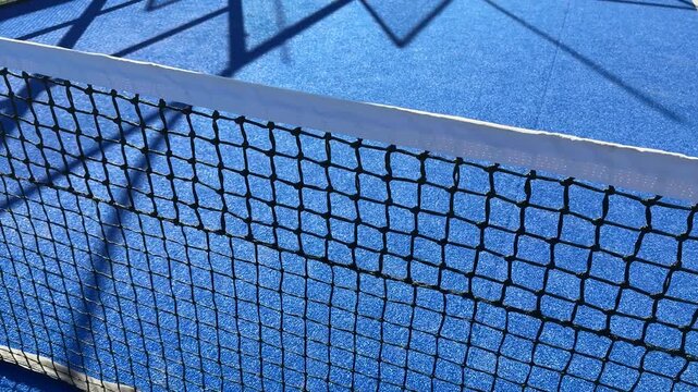 A low angle view looking over a blue netted barrier onto a bright outdoor surface, suggesting a sporting event or park setting, capturing an atmosphere of recreation and activity
