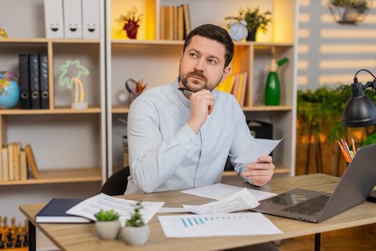 Young man on home table reads contract pages and marks key lines before signature at home. Adult guy on home table carefully checks details in official document and thinks about terms on work laptop.