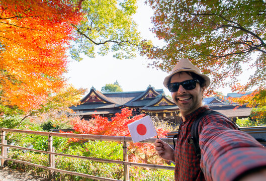 Male tourist taking a selfie with a beautiful panoramic view and vibrant autumn foliage at a Japanese temple in Kyoto.