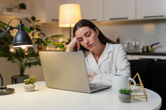 Young woman at night home feels burnout wants pause takes breath after work on laptop. Caucasian girl on sofa at table at evening looks tired says enough rubs temples needs break rests eyes closed.