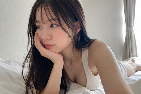 ベッドに横たわり横を見る白いタンクトップの女性