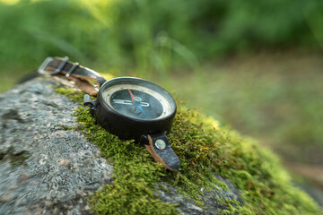 Vintage compass resting on moss covered rock in a forest. Navigation equipment for hiking, exploration, adventure, outdoor travel, direction, and discovering nature with copy space. © Svetliy
