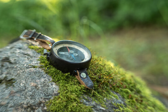 Vintage compass resting on moss covered rock in a forest. Navigation equipment for hiking, exploration, adventure, outdoor travel, direction, and discovering nature with copy space.