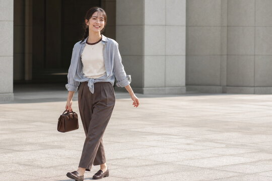 明るい広場を軽い青灰シャツで歩く笑顔の女性