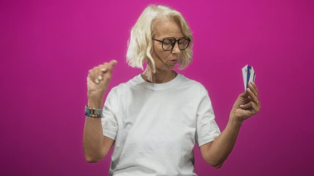 Woman blonde middle age wearing glasses and white t shirt holding multiple creditcard cards, points finger to cards in studio; decision.
