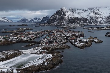 Aerial winter view of the iconic Henningsvaer football field in Norway’s Lofoten Islands, surrounded by snow-covered rocky islets, Arctic sea and dramatic mountains. © JEREMIE