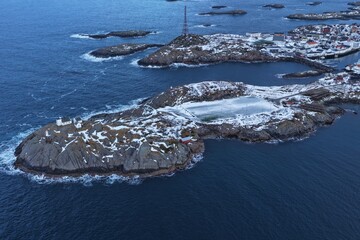 Aerial winter view of the iconic Henningsvaer football field in Norway’s Lofoten Islands, surrounded by snow-covered rocky islets, Arctic sea and dramatic mountains. © JEREMIE