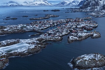 Aerial winter view of the iconic Henningsvaer football field in Norway’s Lofoten Islands, surrounded by snow-covered rocky islets, Arctic sea and dramatic mountains. © JEREMIE