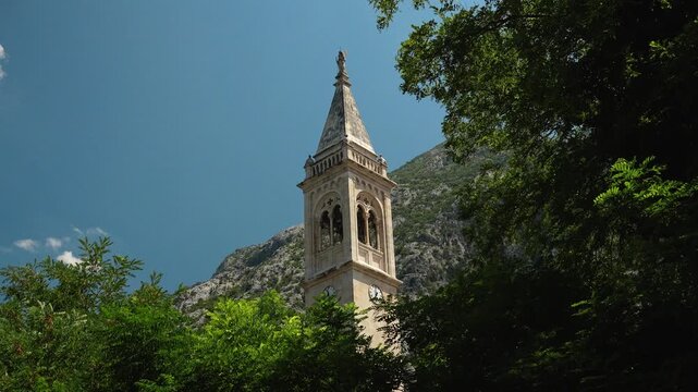 Historic bell tower of the Church of St. Eustahije framed by Mediterranean trees in Dobrota. Architectural landmark of Boka Bay in Montenegro