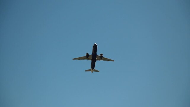 Commercial passenger airplane captured from below against a clear blue sky. Minimal aviation background with copy space