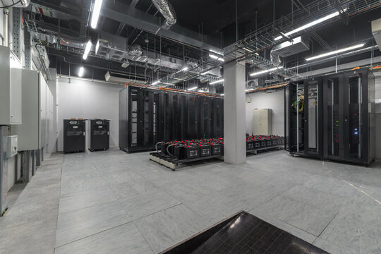 Inside a data center, several server racks are arranged along the walls. Equipment is stored on the floor. The setting has bright lighting and a clean layout