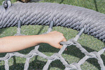 Close up hand holding grey woven rope basket nest swing on outdoor playground for sensory play tactile activity and active childhood leisure concept © Marina