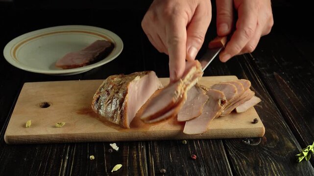 Chef slices cooked meat on wooden cutting board with knife, placing slices onto white plate, showcasing the process of preparing food in a kitchen setting with dark wooden background
