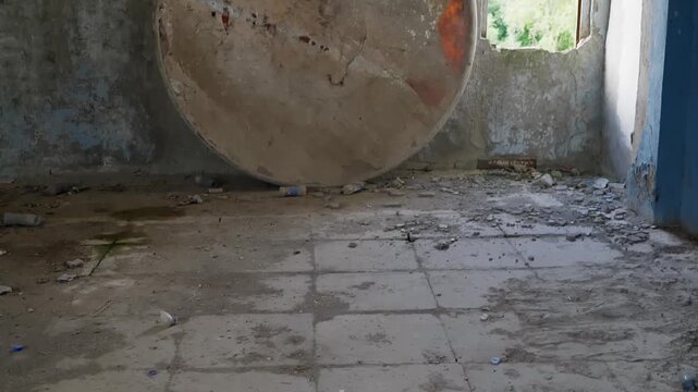 Massive circular storage tank sits in dilapidated interior space with weathered walls, rust stains, scattered debris, industrial decay suggesting neglect, abandonment.