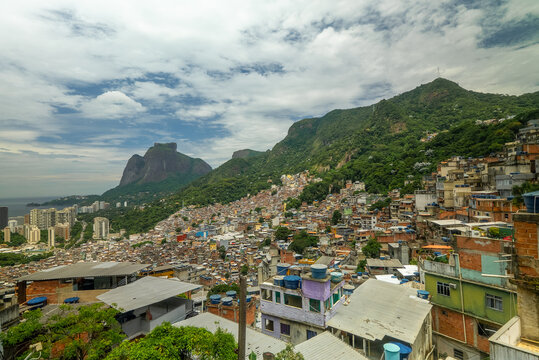 View of the dense urban landscape of Rocinha favela, featuring stacked brick houses and narrow alleyways set against lush green mountains in Rio de Janeiro, Rio de Janeiro, Brazil.