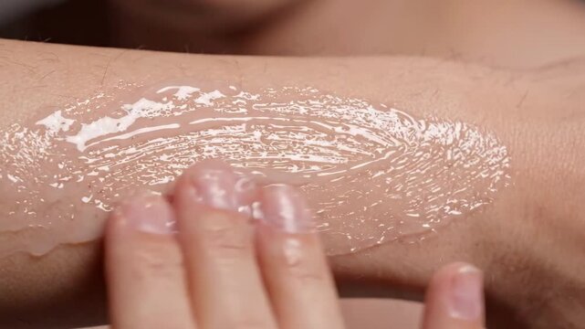 Skincare application: A close-up shot of fingers applying a translucent skincare product to the back of a hand, showcasing the product's texture and absorption.
